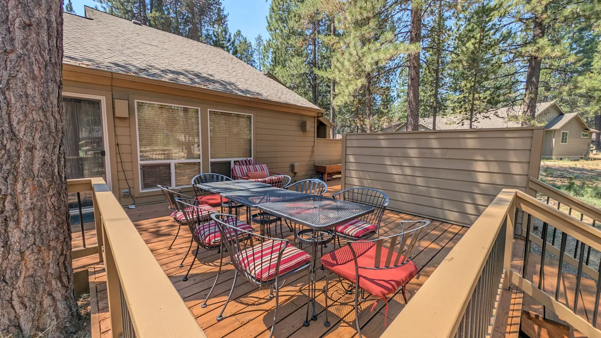 An inviting outdoor dining area set amidst lush trees, featuring a cushioned table and chairs on a patio. The space invites groups to gather for meals, play games, or simply unwind together outdoors.
