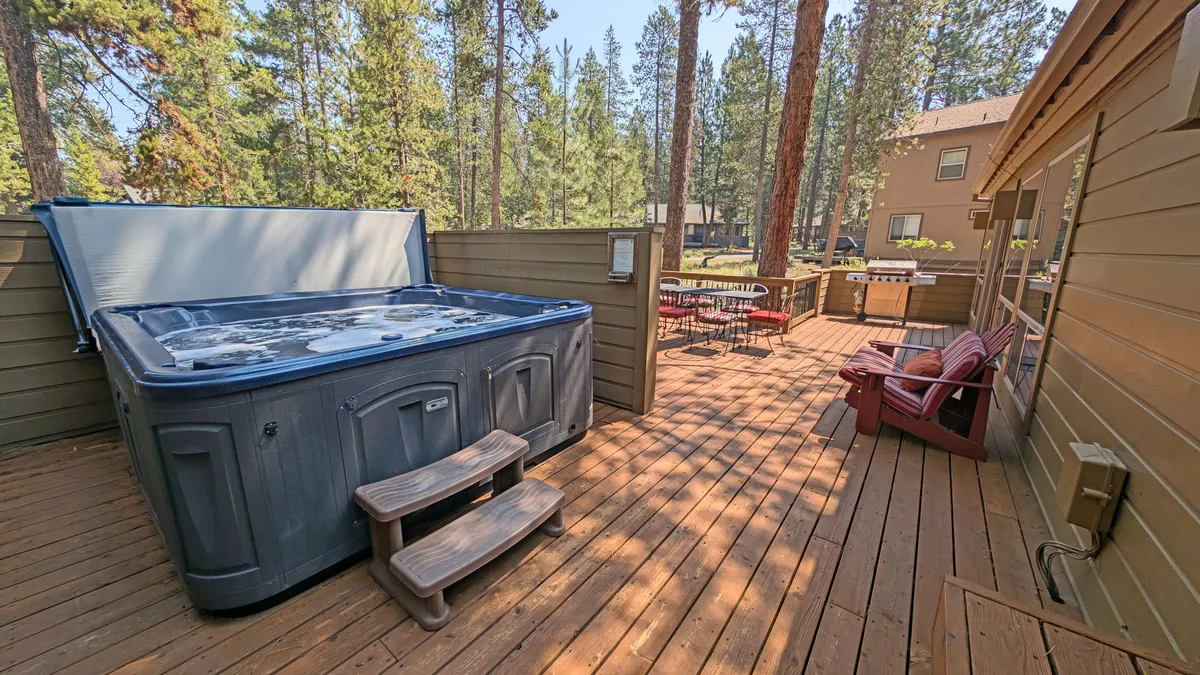This exterior image features a private hot tub on the deck, surrounded by tall trees and comfortable outdoor seating. The scene captures the tranquil setting ideal for relaxing soaks, social gatherings, and enjoying nature views, with hints of evening light suggesting stargazing opportunities.