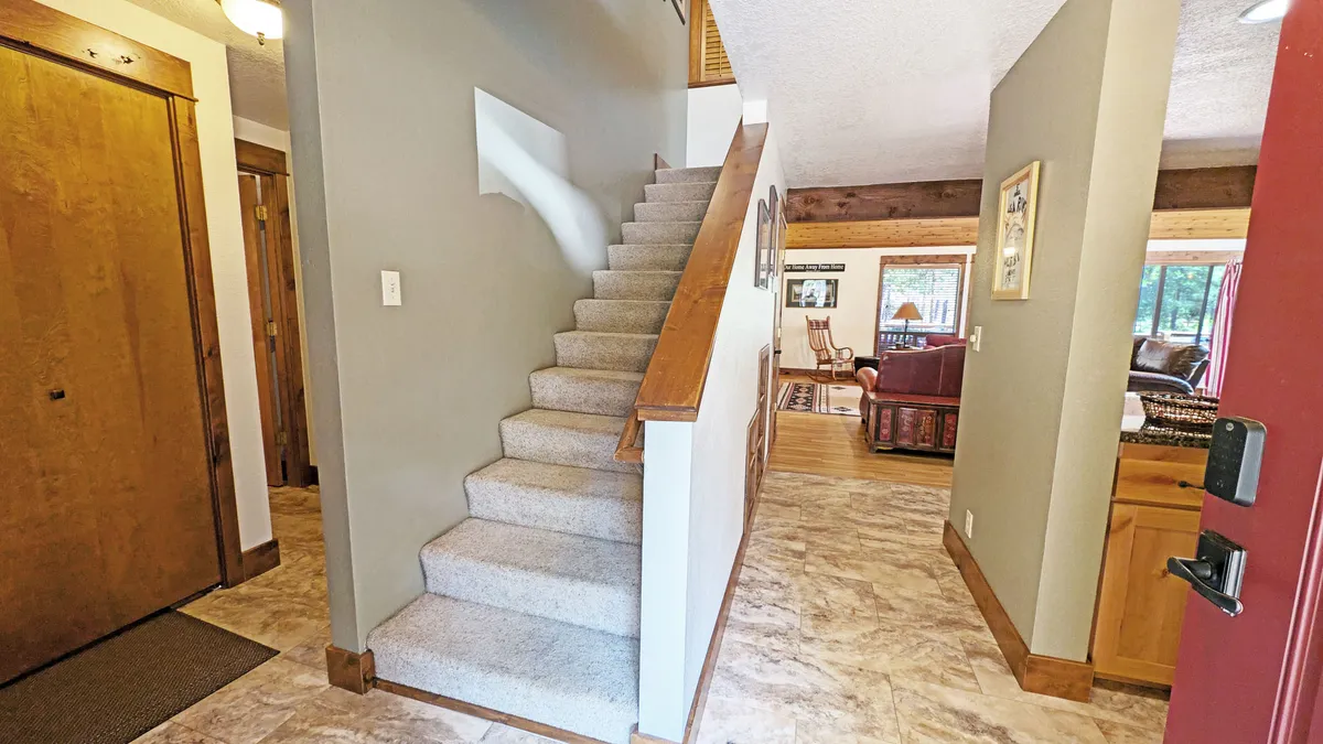 This image captures the entryway of the home, featuring the staircase, front door, and a glimpse into the living and kitchen areas. The scene exudes a welcoming ambiance, with natural light streaming through windows and inviting spaces visible from the threshold.