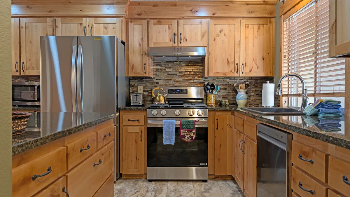 A modern, sunlit kitchen with stainless steel appliances, granite countertops, and rich wooden cabinetry. A decorative backsplash adds style, while the open layout and peninsula seating invite conversation and casual dining.
