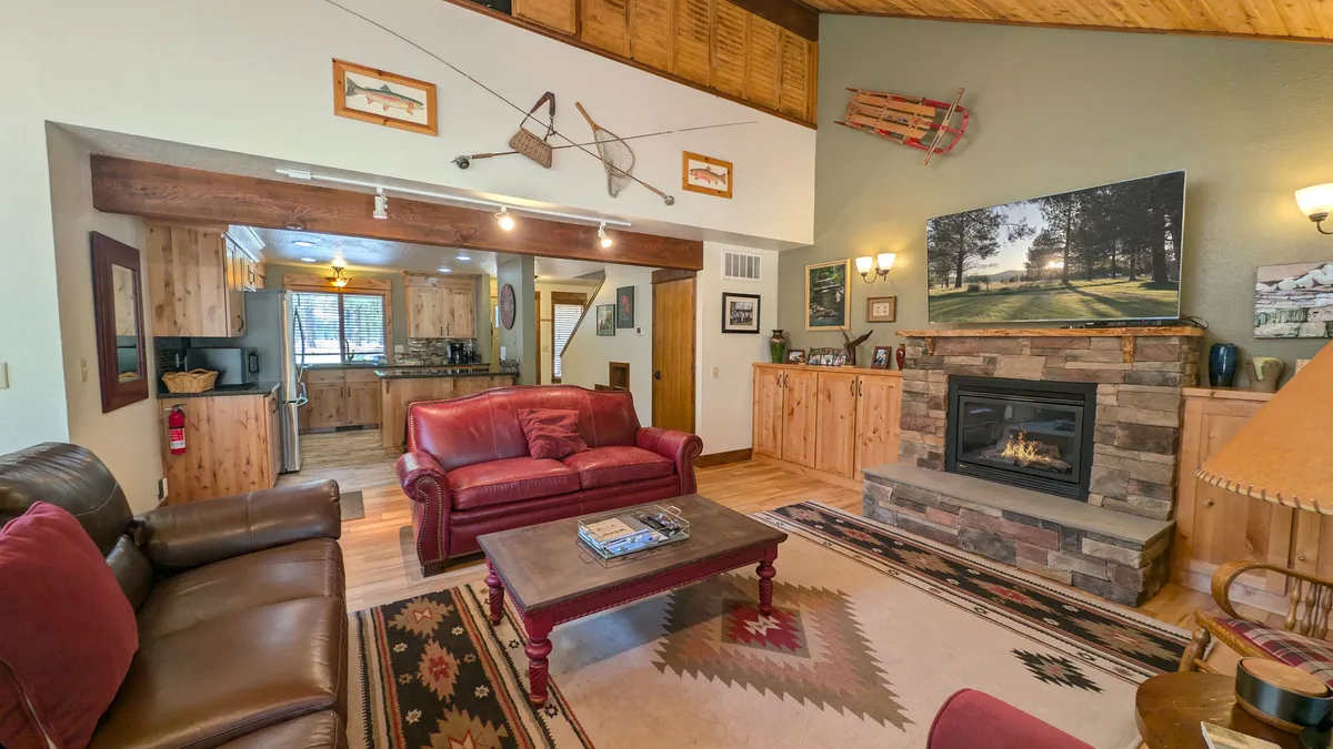 A cozy seating area centered around a fireplace, with wooden cabinets and decorative artwork, offering a warm spot to unwind. The space features comfortable seating and hints at adjoining rooms, suggesting a welcoming flow for family and friends.