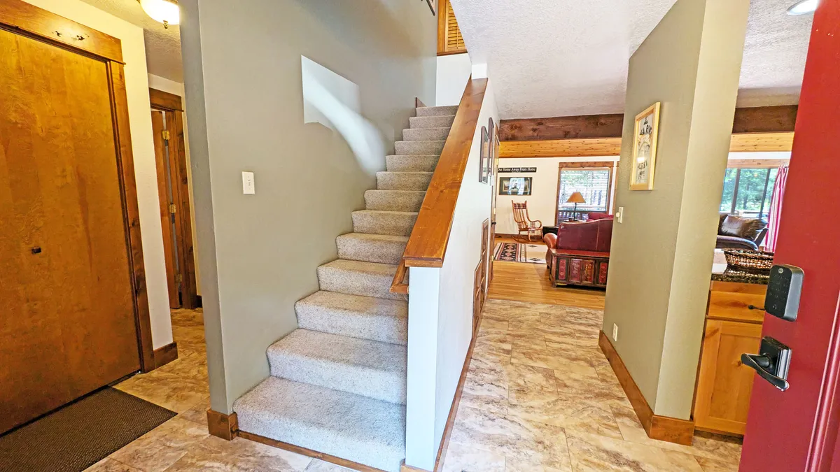 A view of the interior staircase, doorway, and a sunlit living area, capturing the inviting transition between spaces. The ambiance is warm and highlights gathering points for family and friends to regroup between adventures.