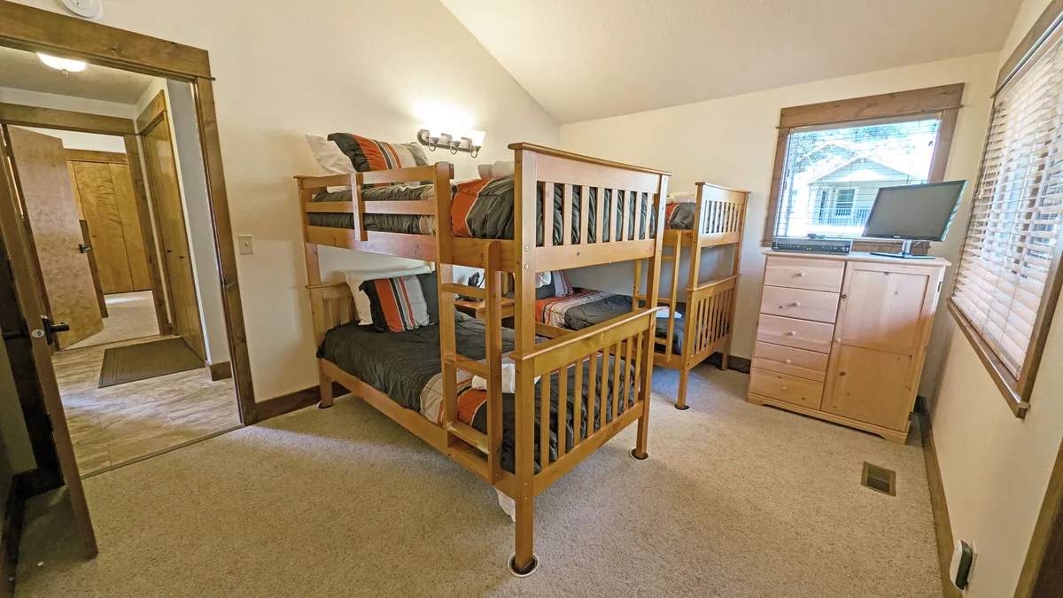 A cozy bunk room featuring multiple bunk beds, a television, a dresser, and a window with a view. The space feels casual yet inviting, ideal for sleepovers or group stays, and offers plenty of entertainment for younger guests.