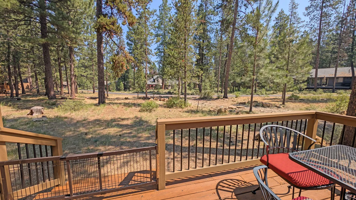 A view from the deck shows outdoor seating surrounded by tall trees, a distant cabin, and natural beauty, suggesting an inviting space for gatherings or peaceful reflection after adventures.